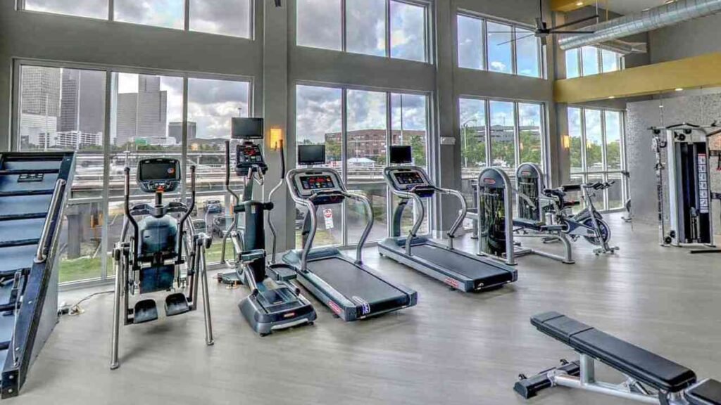 A sleek, modern apartment living room with foldable cardio machines like a treadmill, elliptical, and exercise bike neatly placed