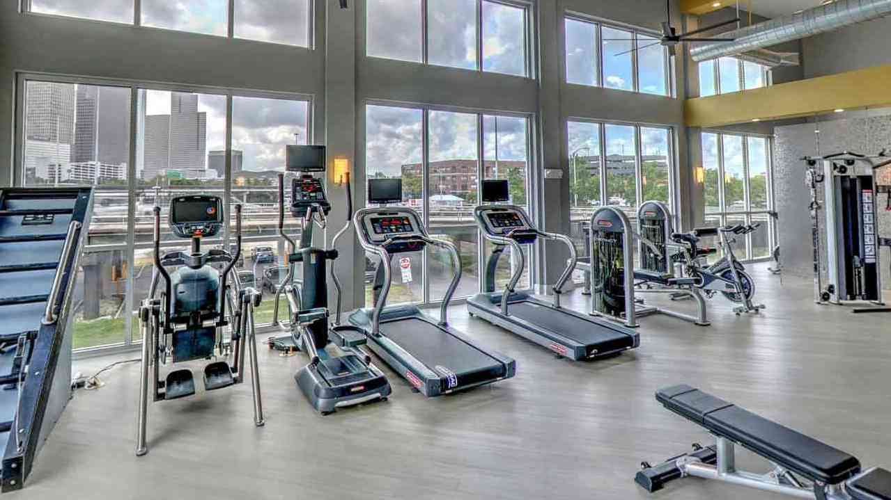 A sleek, modern apartment living room with foldable cardio machines like a treadmill, elliptical, and exercise bike neatly placed